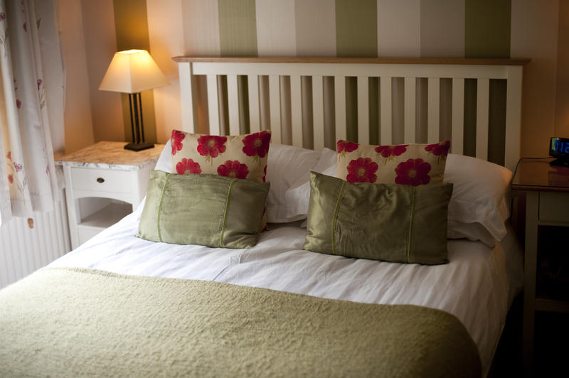 Homely bedroom with a wood framed bed with a slatted headboard and pretty floral cushions