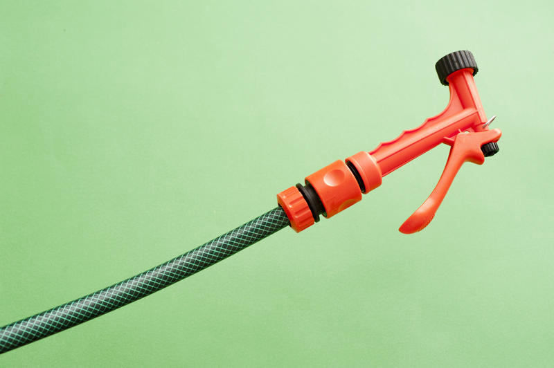 Orange plastic garden sprayer on a green hosepipe for spraying a fine jet of water onto germinating seeds and delicate plants, on green with copyspace