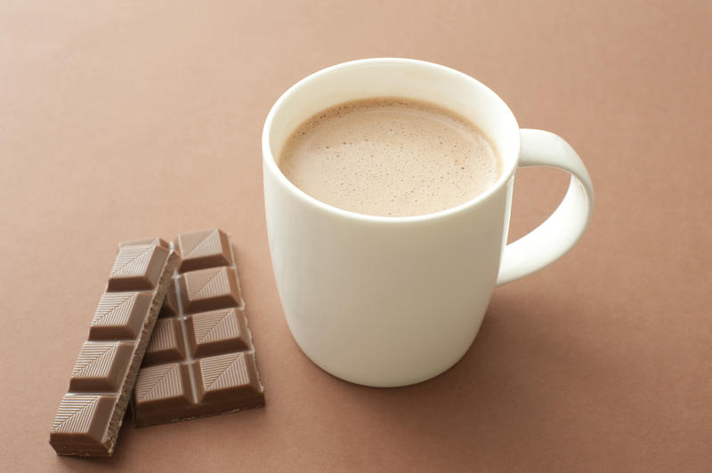 White mug of cacao and milk chocolate on brown background.