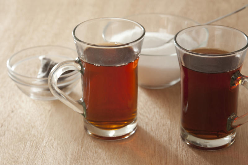 Two glass mugs of freshly brewed hot black tea with a bowl of sugar and the used teabags behind, high angle view