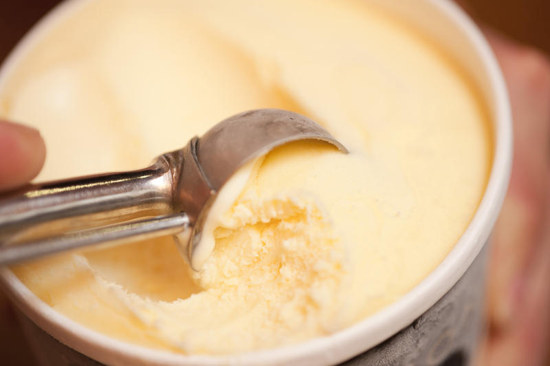 Person serving refreshing ice cream from a bowl using a metal scoop for a tasty summer dessert