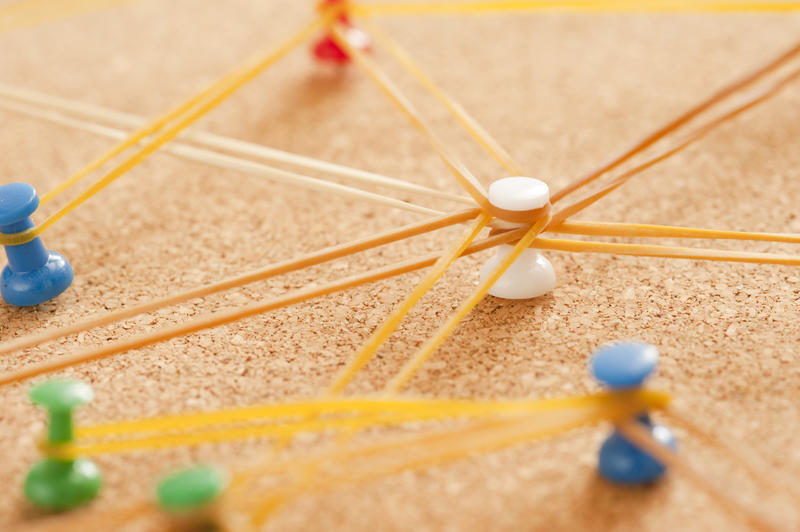 Close Up of Colorful Thumb Tacks in Cork Board Connected with Stretched Rubber Bands