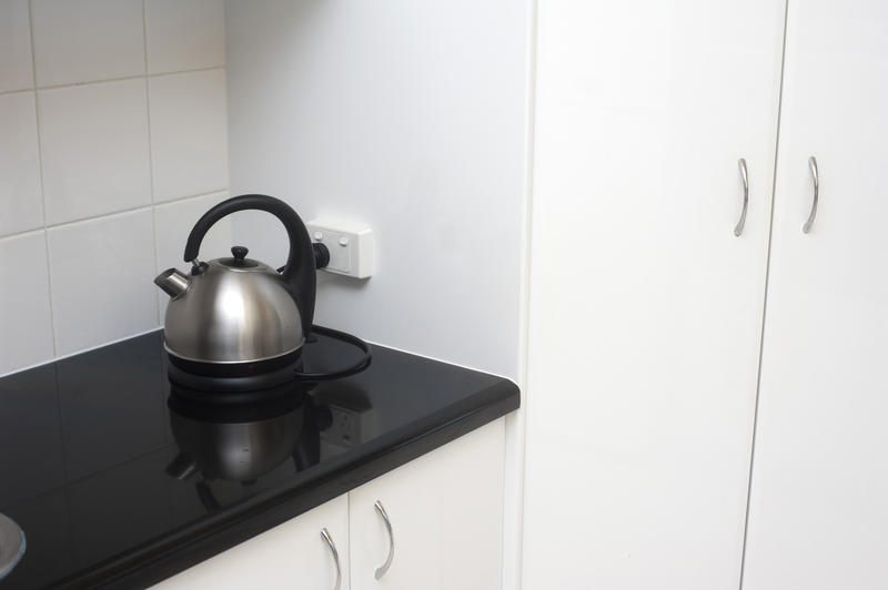 Modern electrical silver domed domestic kettle standing on a black countertop in a white tiled kitchen