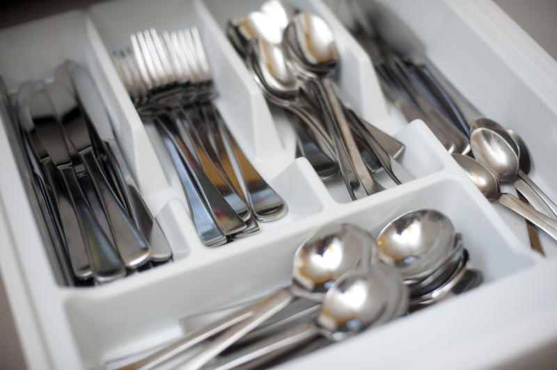 Interior of a kitchen cutlery drawer with internal divisions for the neat storage of a set of silver metal cutlery consisting of knives, forks and spoons