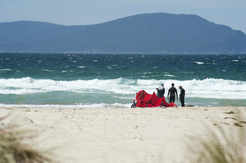 Group of kite surfers in wetsuits preparing the kite board on a sandy tropical beach with a rough ocean and mountains