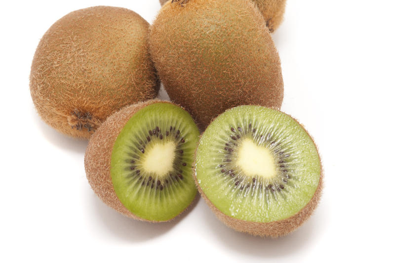 Fresh whole and halved kiwifruit on a white background showing the texture of the juicy green pulp and arrangement of the pips