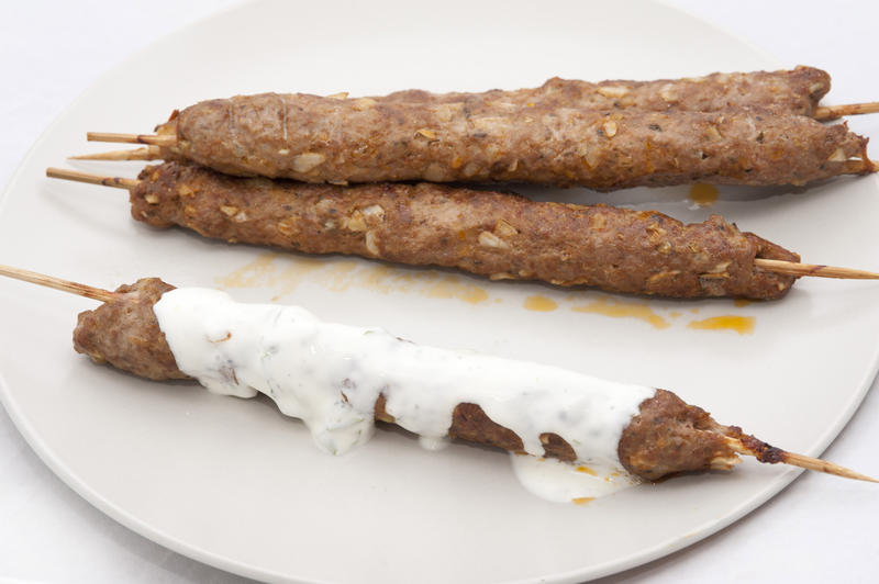 Grilled kofta kebabs made from spiced minced lamb cooked on a skewer drizzled in spicy yoghurt sauce served on a plate