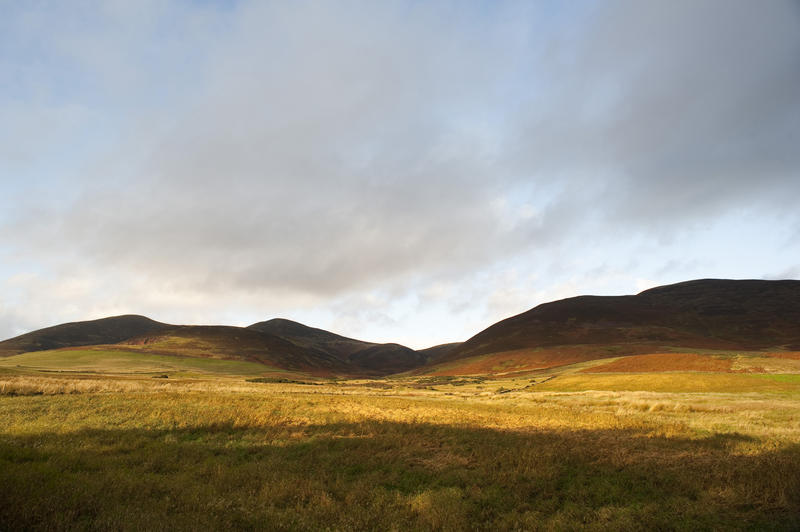 Panorama View of Relaxing Grassy Landscape with Hills Under Stormy Sky