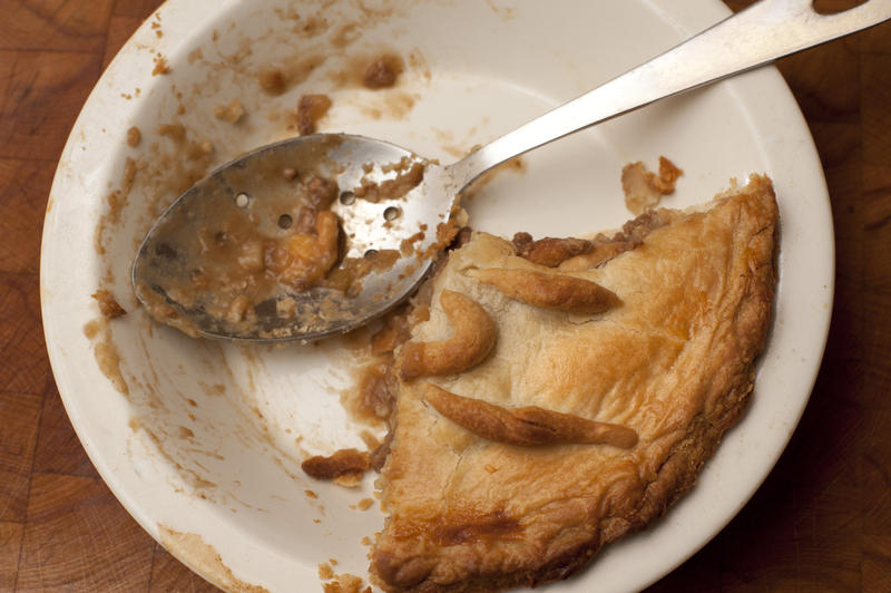 Remnants of a half eaten large pie in a dish with a dirty serving spoon, view from above