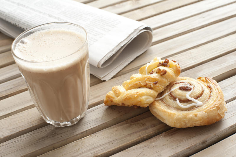 Cup of delicious hot cacao, two buns and fresh newspaper on wooden table