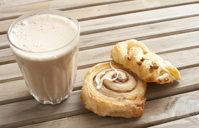 Latte snack with a glass of milky frothy coffee ad two Danish pastries on a slatted wooden table outdoors, close up high angle view