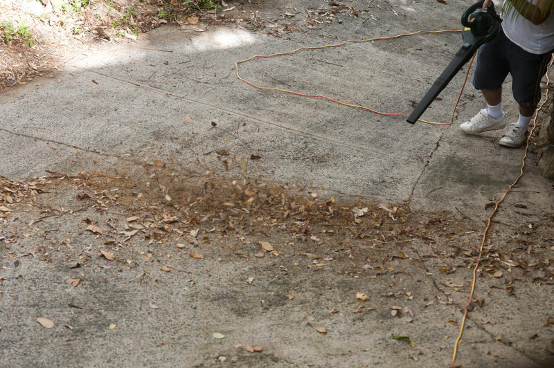 Man operating a leaf blower to clear the dead autumn leaves off paving in the garden, view showing his feet and the nozzle of the tool