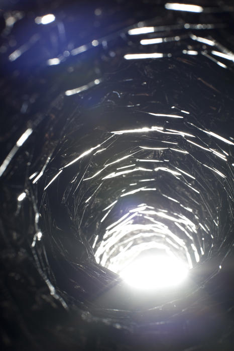 Ray of light passing through a tunnel with a view of the rough corrugated internal structure of the tube with bright light flare