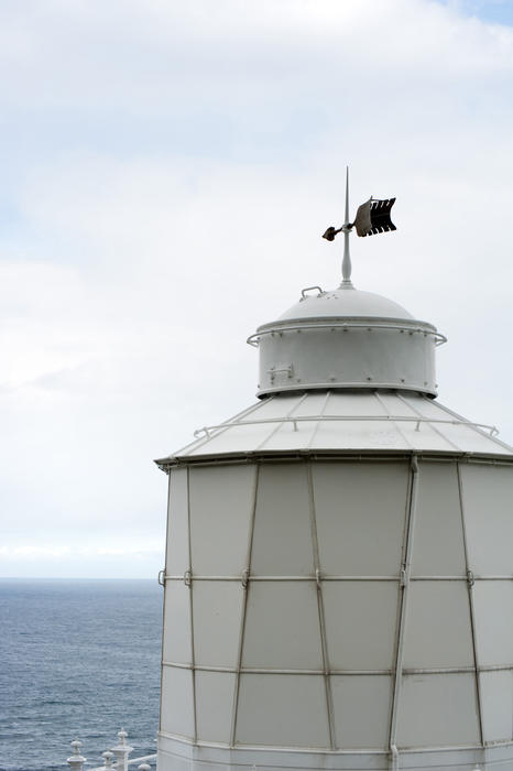 Top of a lighthouse with a weathervane overlooking the ocean providing a guiding light and hazard warning to marine shipping