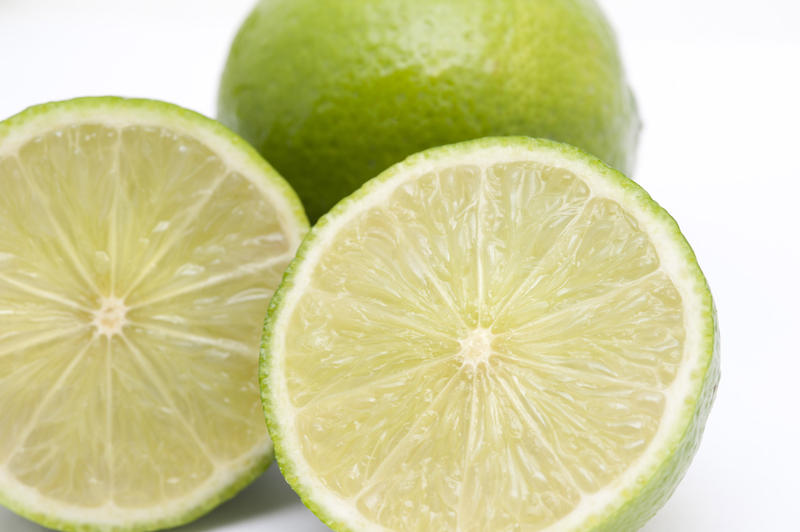 Close-up of two fresh nutritious limes with one cut in two halves in front, on white background