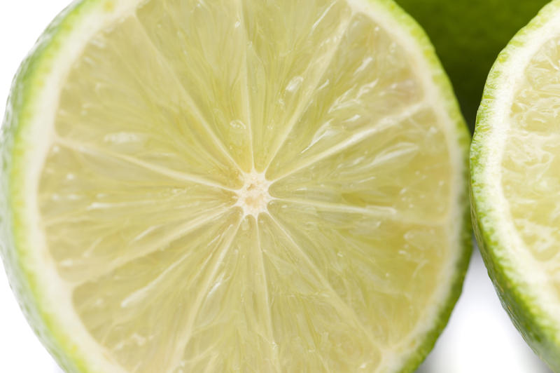 Halved lime detail showing the texture of the juicy pulp, rind and segments over a white background