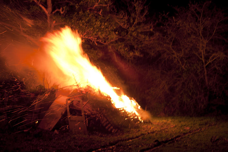 Lit bonfire taking hold on the wood and branches with a tongue of orange flame leaping into the night sky in celebration of Bonfire Night