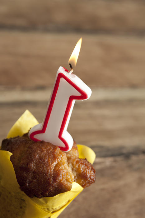 Little first birthday party for a one year old baby with a decorative burning number 1 candle on a festive cup cake over a wooden table