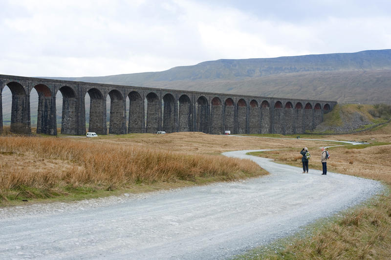 Tthe Ribblehead viaduct, a Victorian railway viaduct which crosses the River Ribble with a view of pedestrians walking on the road below its arches
