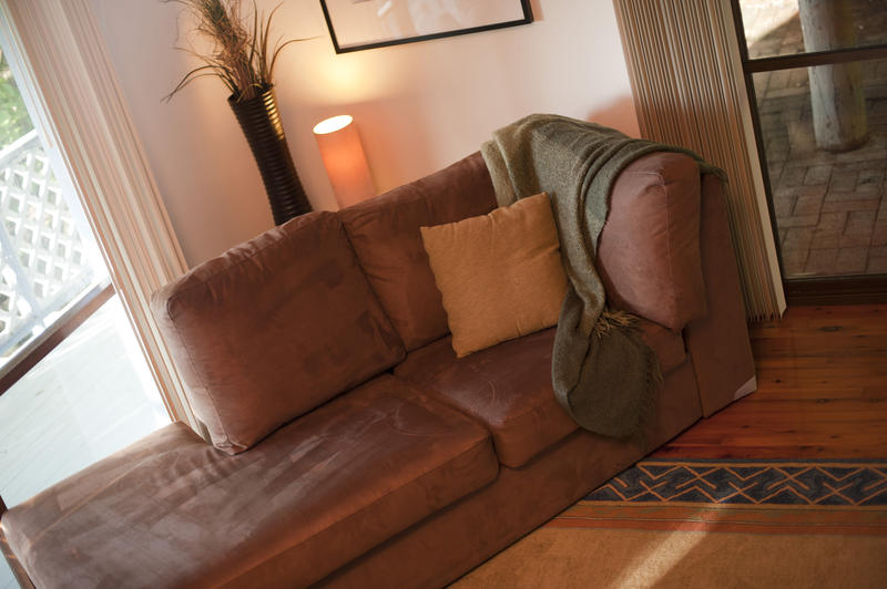 Angled settee in a lounge with a cushion and throw rug in front of a window leading on to a balcony