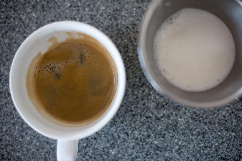 Close-up of two glasses, one with espresso, other with cream, standing on table.