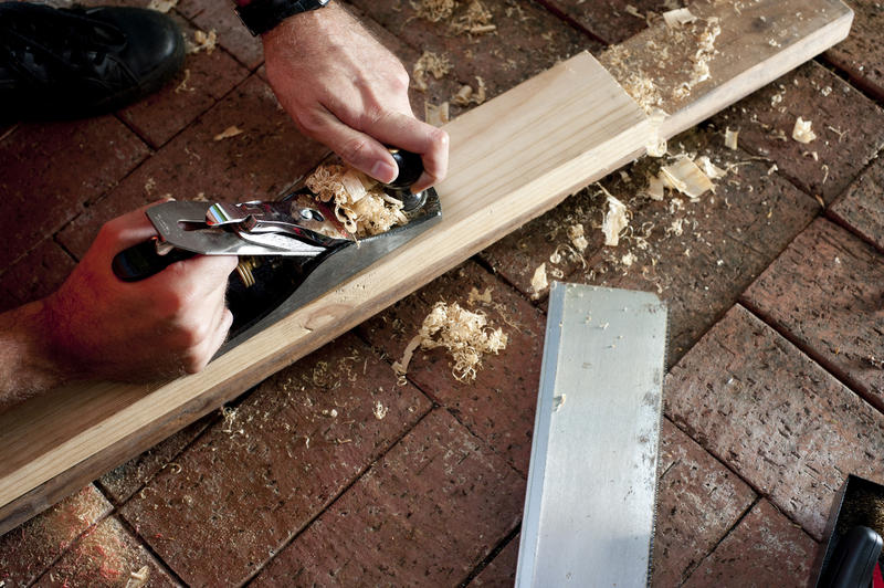 Carpenter using smoothing plane with close up on his hands