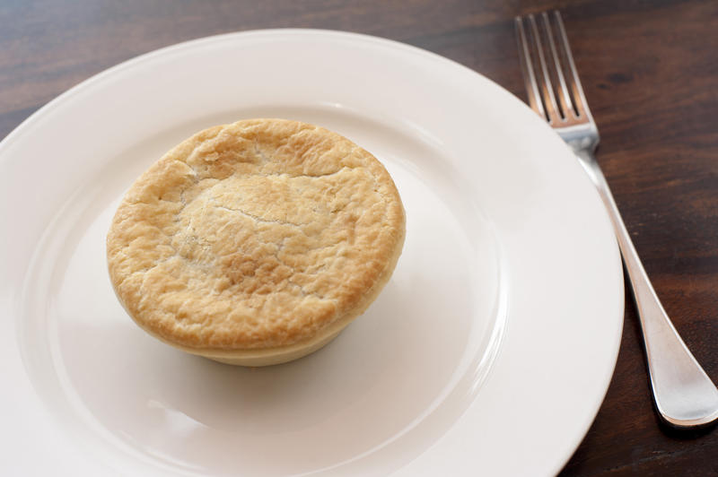 Freshly baked meat pie with a golden pastry crust served on a plain white plate for a snack or lunch