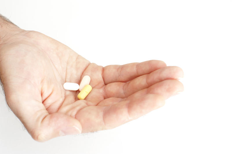 Man holding out his medication in his cupped hand with three different tablets displayed, isolated on white