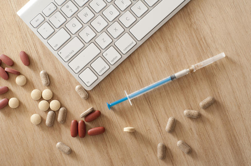 Medical Concept Image - High Angle View of Computer Keyboard Surrounded by Syringe and Variety of Pills and Tablets