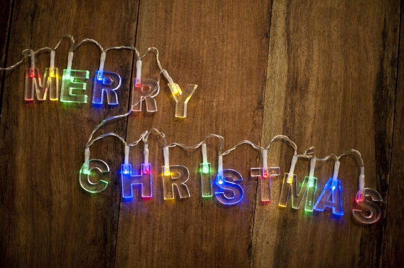Merry Christmas lights with the words formed of colorful letters on a garland or string placed over a wooden table to wish people a happy holiday season