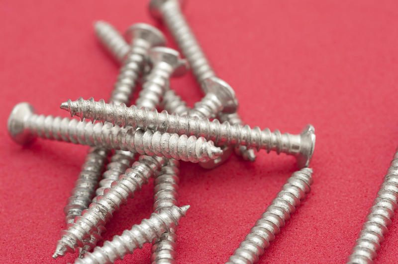 Scattered full thread metal woodworking screws on a red background with copyspace in a DIY concept