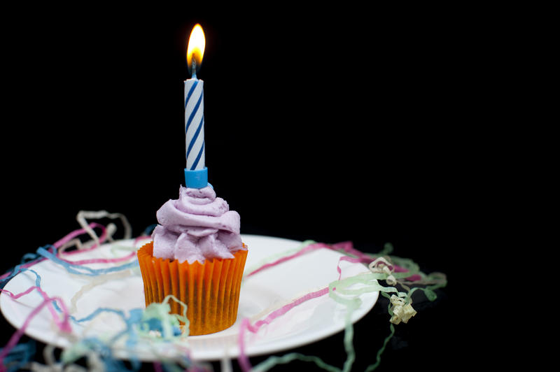 a small decorated cup cake with a candle in in and party streamers
