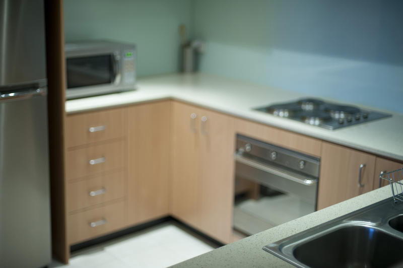 Interior of a small compact kitchen with wooden cabinets, an under counter oven and hob, a microwave and fridge