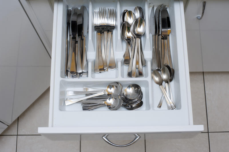Overhead view of silver cutlery in an open kitchen drawer stored neatly in separate divisions