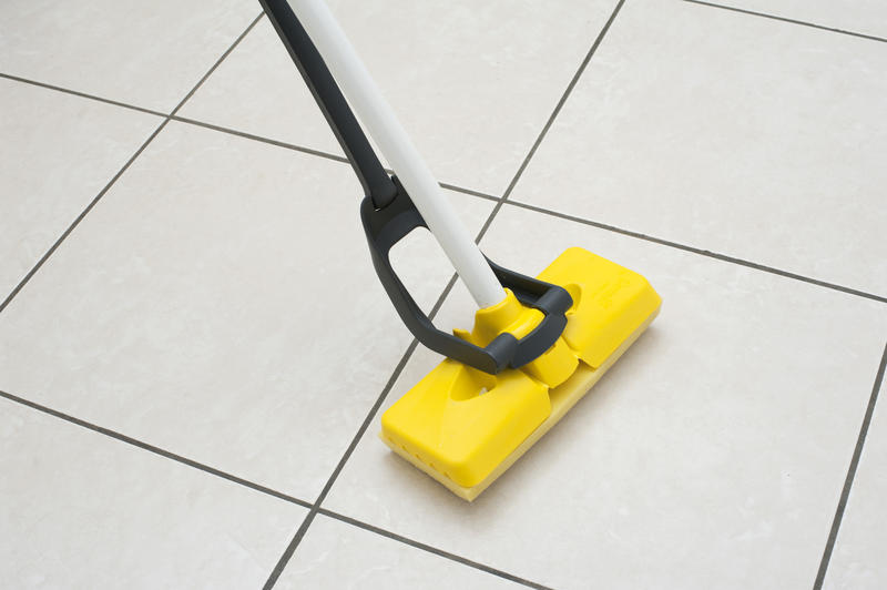 Close up Cleaning the White Tiled Floor with a Yellow Foam Rubber Mop