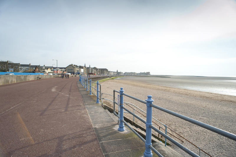 Morecambe seafront with people in the distance walking on the promenade overlooking a wide sandy beach and Morecambe Bay