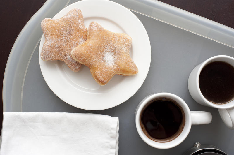 Morning coffee for two with cups of freshly made espresso coffee alongside a plate with two star shaped doughnuts, overhead view of the tray