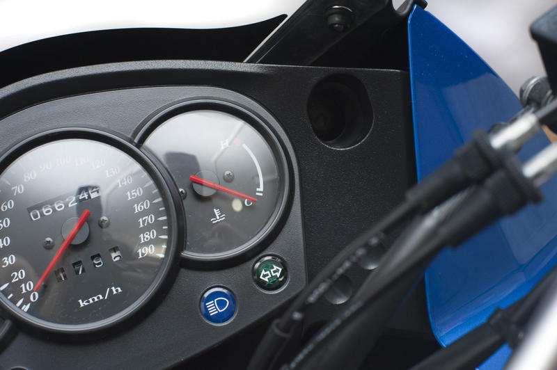 Speedometer and fuel gauges on a motorbike, close up high angle view with light reflection on the glass of the dial
