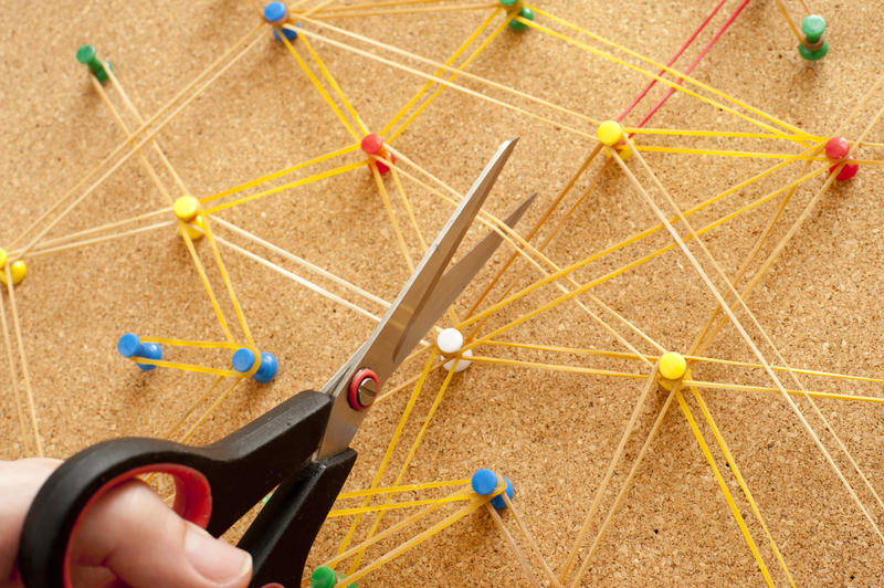 Close up Conceptual Cutting Elastic Rubber Bands Between Pins on a Brown Cork Board Using Pair of Scissors