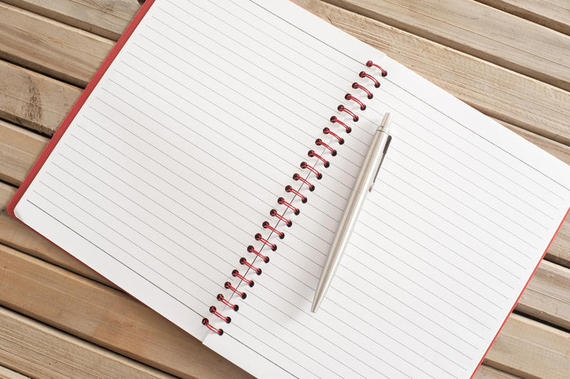 Close up Blank New Page of a Spiral Notebook with Silver Ballpoint Pen, Emphasizing Copy Space for Texts. Placed on Top of Wooden Table.