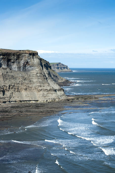 Scenic view over the surf of the North Yorkshire coastline with its rocky cliffs under a clear sunny sky