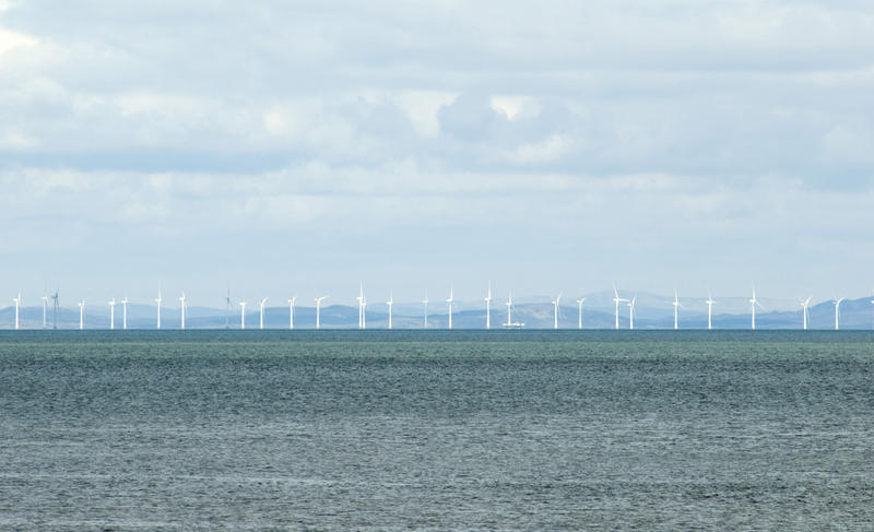 Offshore windfarm with a long row of wind turbines generating electricity from the kinetic energy of the wind near Whitehaven