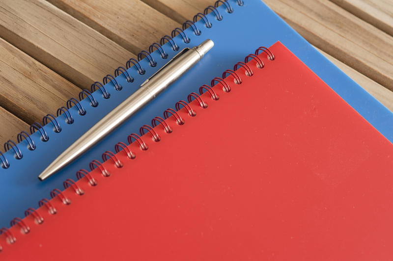 Close up Spiral Blue and Red Office Notebooks with Silver Ballpoint Pen on Top Placed on the Wooden Table.