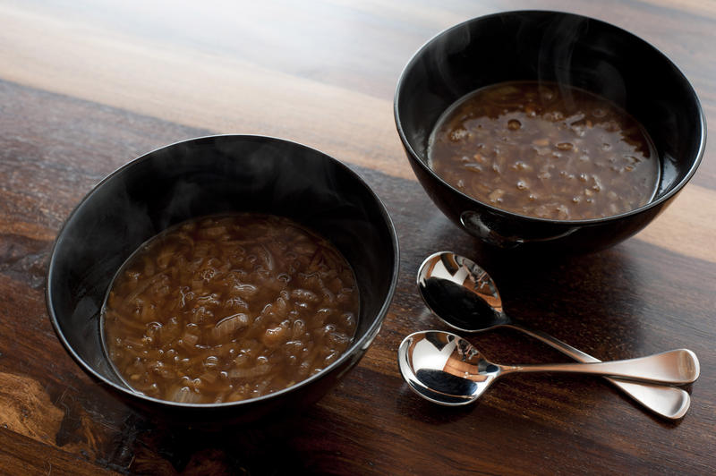 Two bowls of delicious homemade brown French onion soup served as a starter to dinner on a wooden table