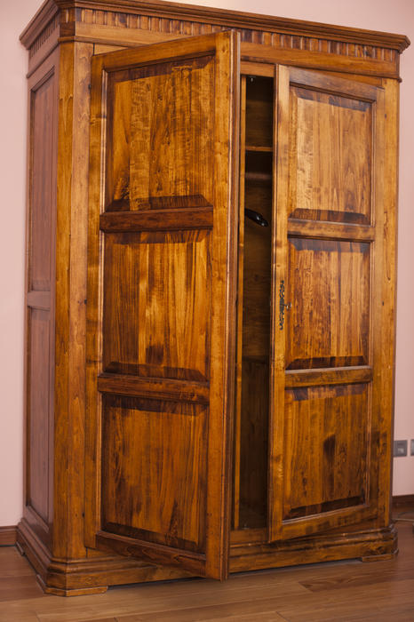 Old rustic wooden wardrobe with paneled doors standing ajar to reveal empty shelves for storage