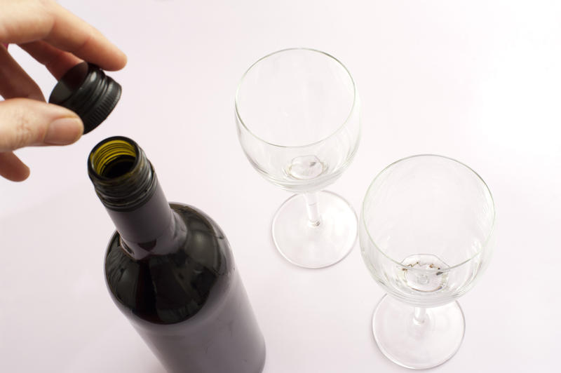 Man opening a bottle of red wine for dinner removing the screw cap in preparation for pouring two glasses standing alongside