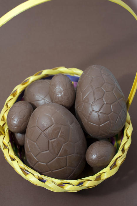 A variety of opened chocolate Easter Eggs in different sizes filling a round wicker basket on a matching brown background