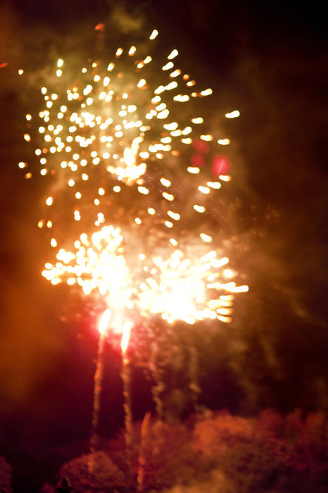 Bursts of orange fireworks lighting up a smoky night sky during a pyrotechnics display on Bonfire Night or Guy Fawkes