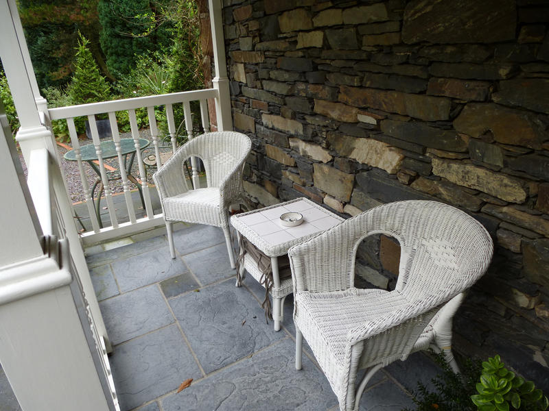 White outdoors furniture with two armchairs and a coffee table on the porch of a rustic stony house