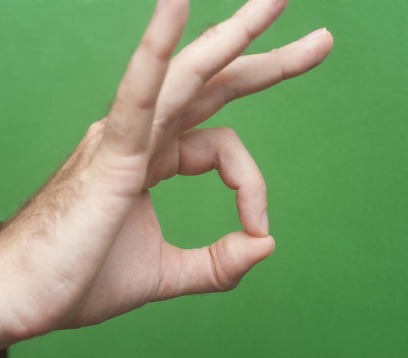 Man making a perfect gesture with his fingers over a green background to signal his complete satisfaction with a quality service or product